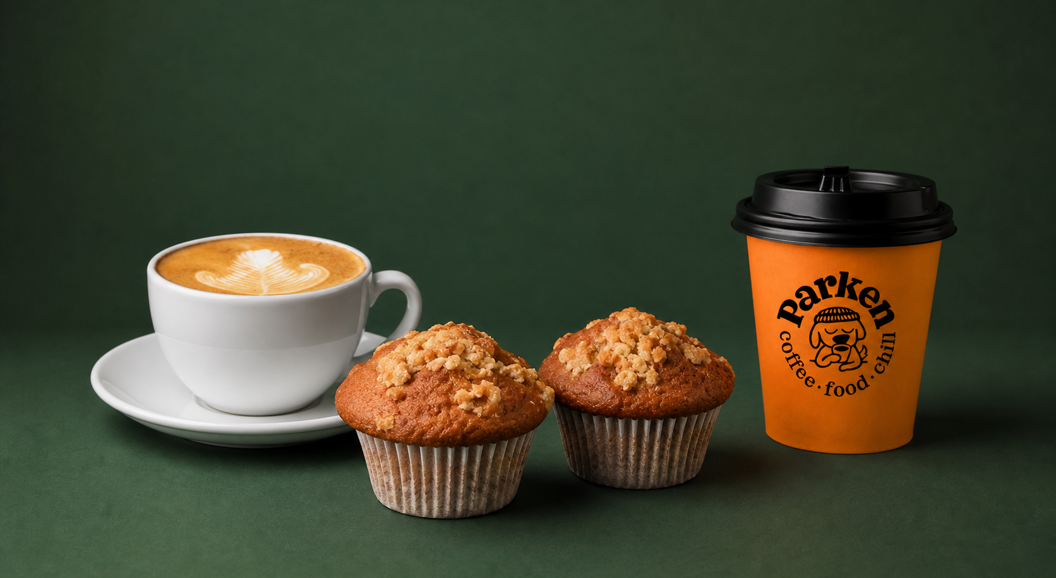Kaffekopp med cappuccino, to muffins og en takeaway kaffekopp fra Parken Coffee på grønn bakgrunn