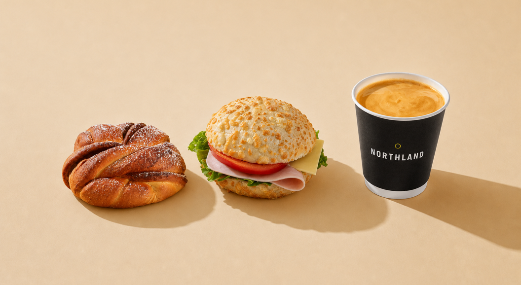 Kanelsnurr, sandwich med skinke og ost, og kaffe i svart kopp fra Northland på lys bakgrunn