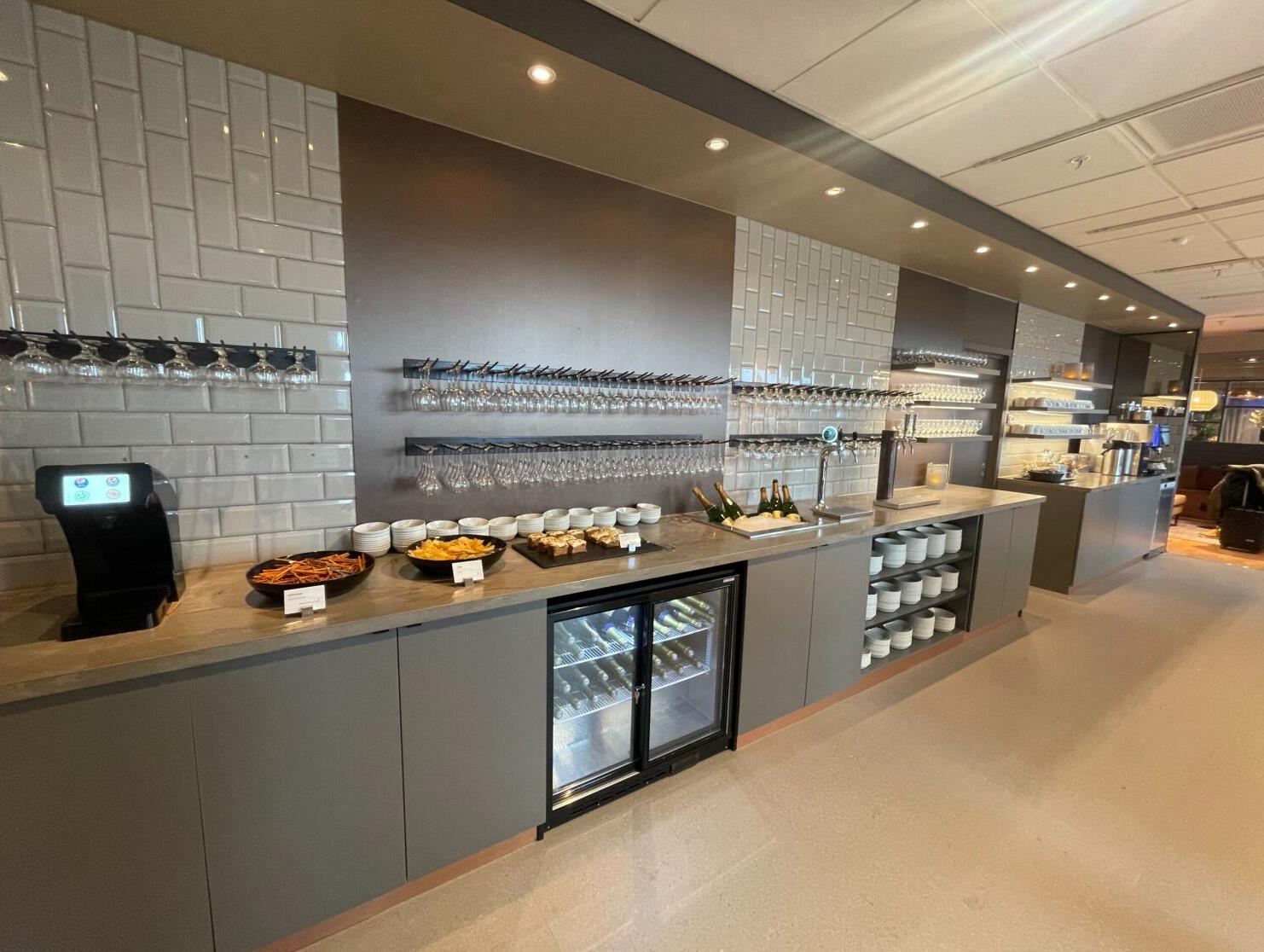Moderne buffetoppsett i en lounge med drikkedispenser, ulike forretter, hengende glass, og arrangerte tallerkener, som forbedrer spiseopplevelsen