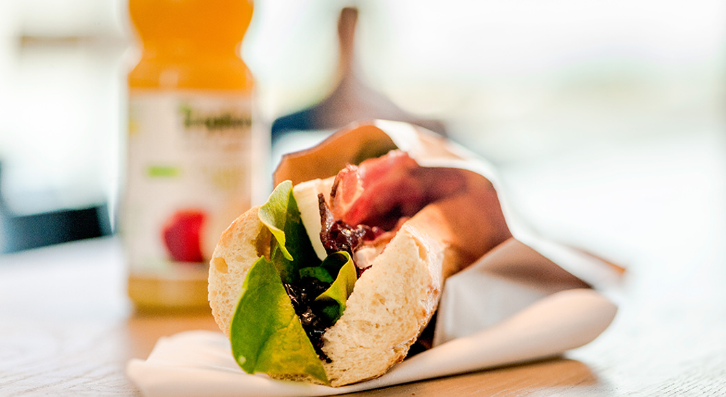 Nylaget sandwich med salat, bacon og ost på et trebord, ledsaget av en flaske appelsinjuice i bakgrunnen