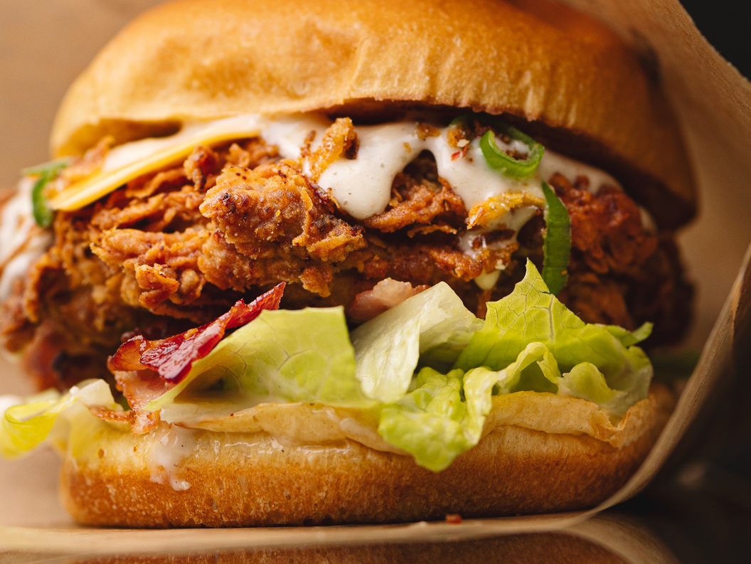 Nærbilde av en sprø, fritert kyllingsandwich med salat, bacon og kremet saus på en ristet hamburgerbrød