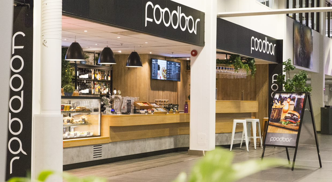 Moderne matbarinteriør med trebardisker, sorte pendellamper og en digital menyvisning. A-skilt med et burgermåltid i forgrunnen