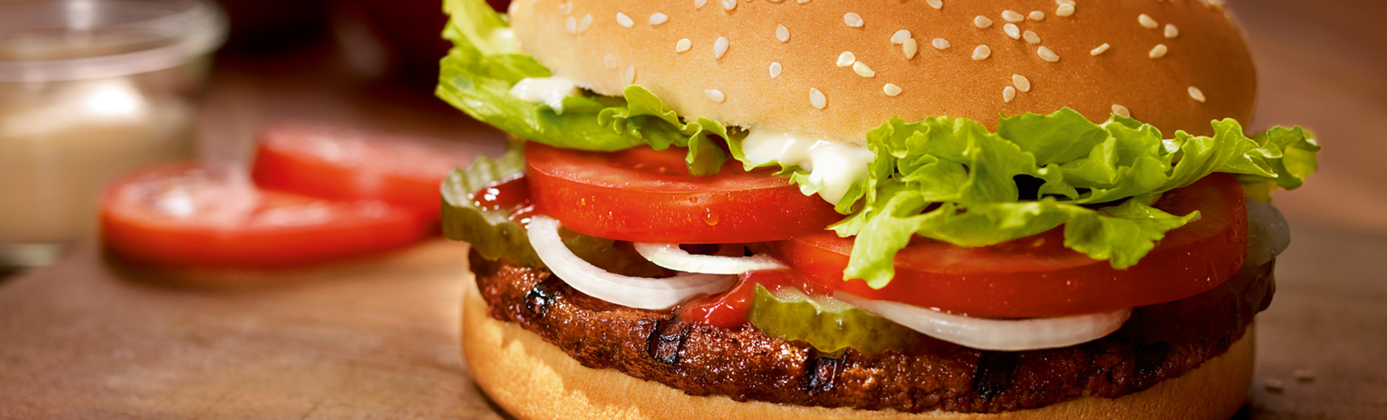 Saftig hamburger med salat, tomat, løk og sylteagurk på ein treplate