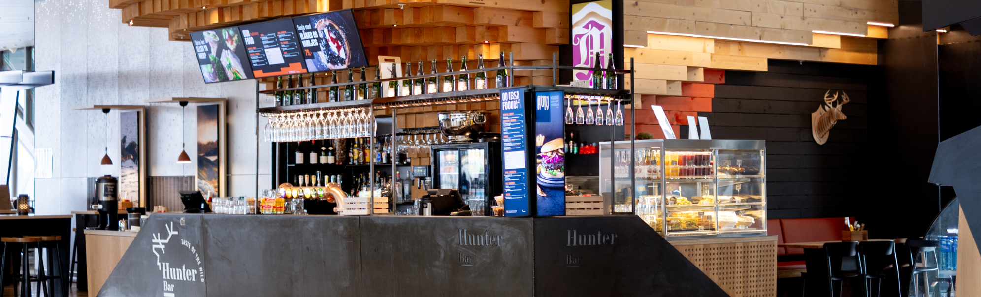 Moderne kafe med tresøyler og glasmonter, serverer drikke og snacks i ein flyplasslounge