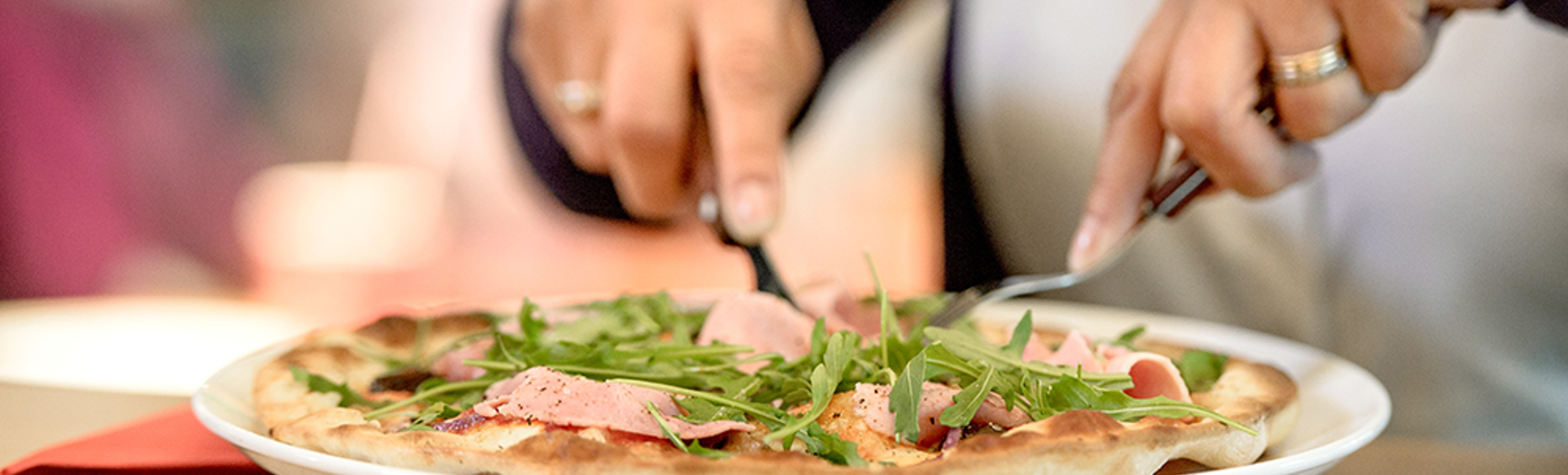 Person et pizza med ruccola og skinke med kniv og gaffel