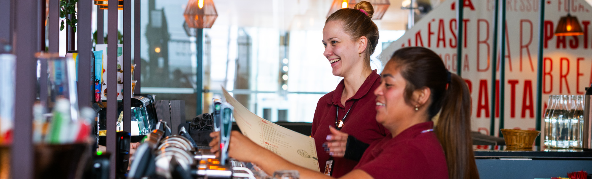 To servitørar arbeider saman bak ein bar i ein restaurant, omgitt av glas og moderne belysning