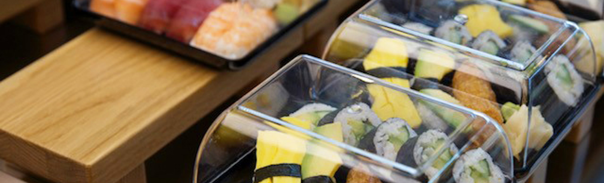 Sushi i plastboksar på utstillingsbord, med variasjonar av nigiri og maki med fersk laks, tunfisk og egg