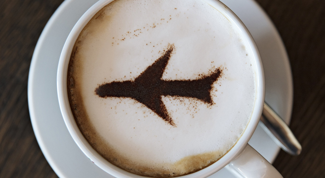 Cappuccino med flydesign i kanel på skummet melk, servert i en hvit kopp og skål på et trebord