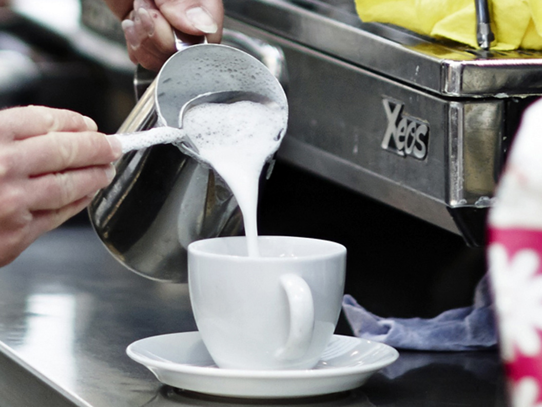 Barista expertly pouring steamed milk into a white cup in a coffee shop setting