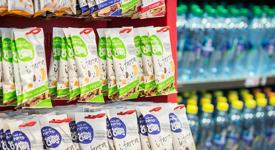 Snacksposer på en rød butikkhylle, ved siden av en kjøler med flaskevann i en butikksetting