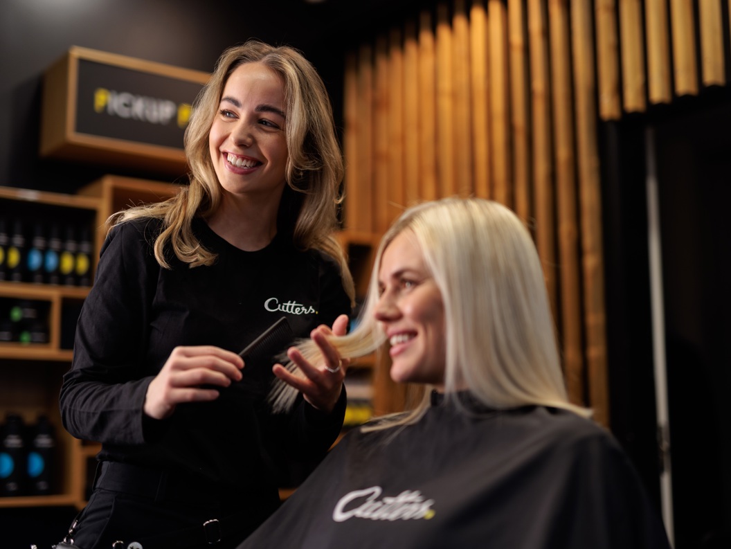 Frisør med langt hår som smiler mens hun hjelper en blond kunde i en moderne salong
