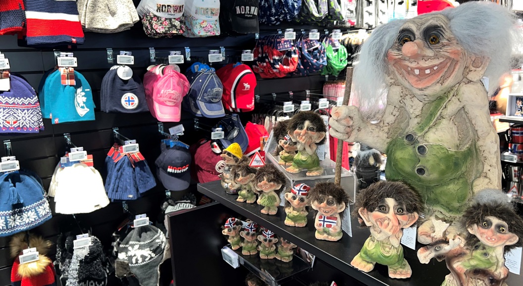 Trollfigurar og suvenirar med norske motiv i ein butikk, omringa av ulike luer og kapsar med Noreg-tema