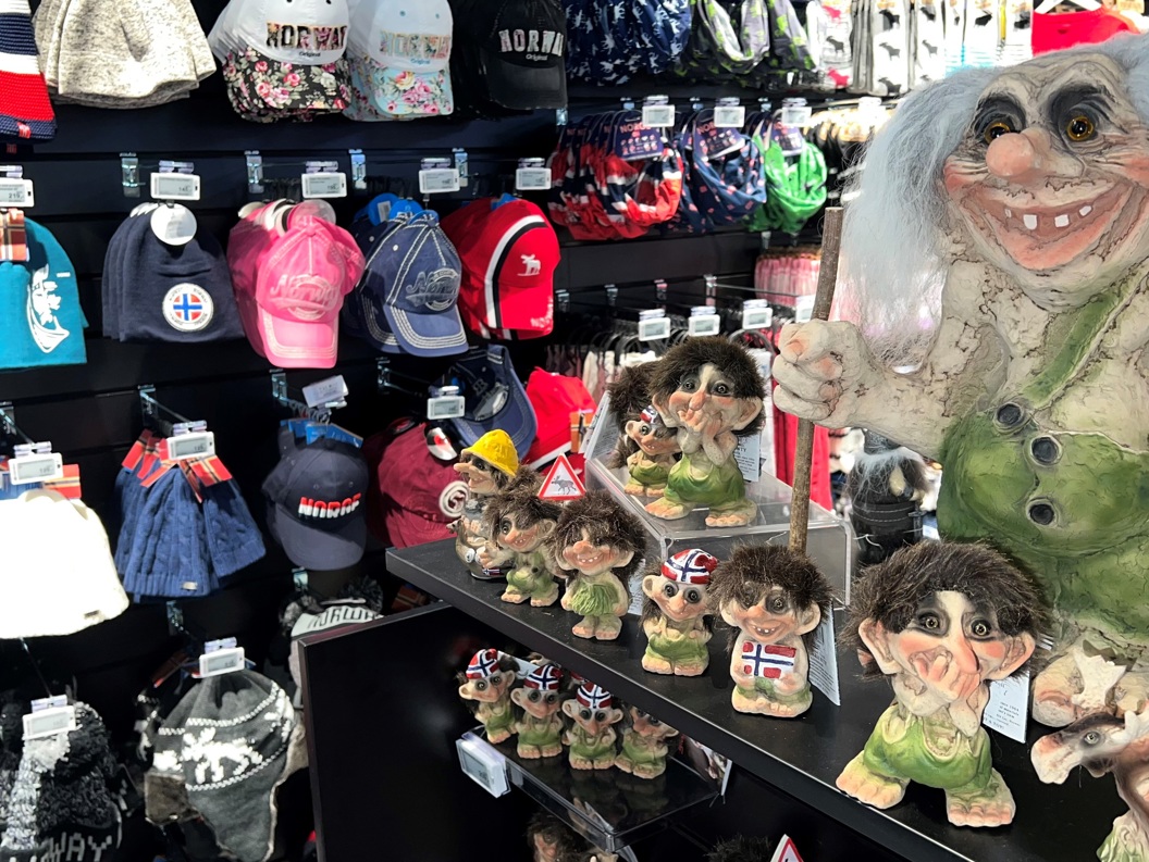 Trollfigurar og suvenirar med norske motiv i ein butikk, omringa av ulike luer og kapsar med Noreg-tema