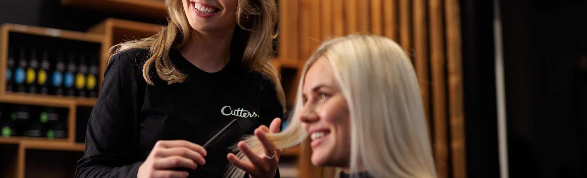 Frisør smiler medan ho friserer ein kunde med langt blondt hår i ein moderne frisørsalong