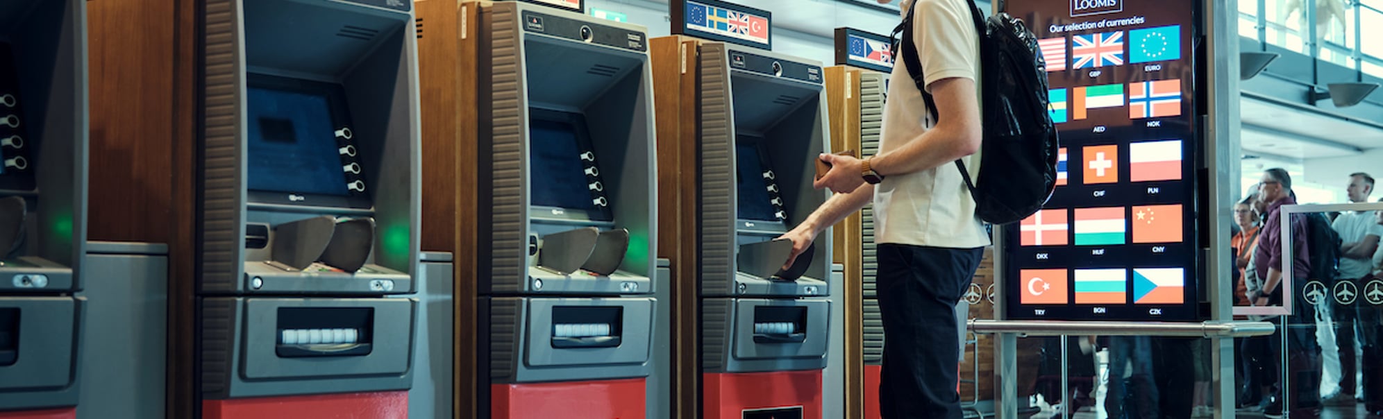 Mann tar ut pengar frå ein minibank på ein flyplass, ved sidan av valutakurs-tavle