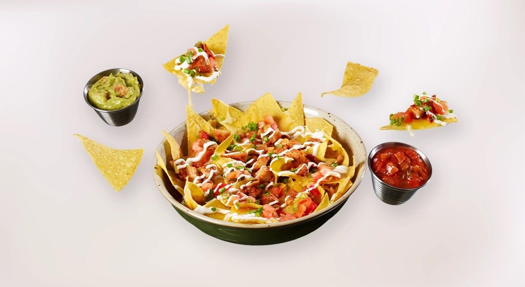 Skål med nachos toppet med salsa, guacamole, ost og rømme, servert med tortillachips på lys bakgrunn