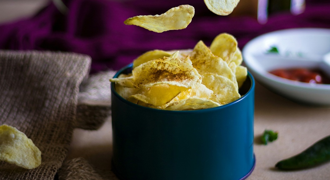 Potetgull i en blå bolle med chips flytende i luften, omgitt av grønne paprikaer og dip i bakgrunnen