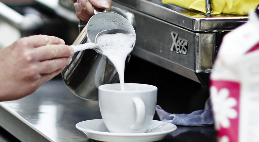 Barista pouring steamed milk into a coffee cup, creating latte art in a cafe setting