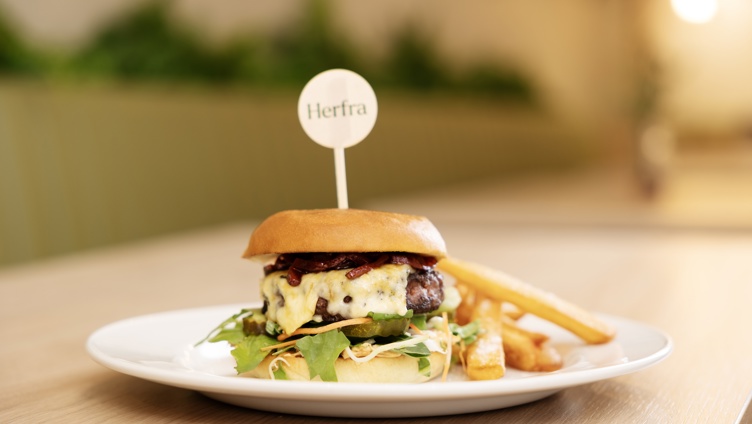 Gourmet cheeseburger på en hvit tallerken med pommes frites, garnert med grønnsaker og toppet med en tannpirker med merkevare, servert på et trebord