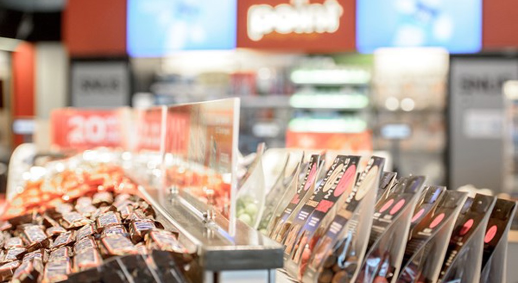 Close-up of neatly arranged snack displays at a convenience store checkout, featuring a variety of packaged chocolates and candies, with a blurred background showing store signage and shelves
