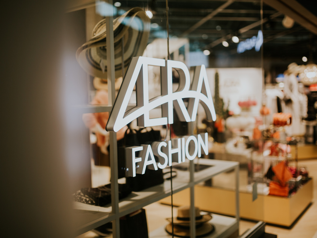 Illuminated "VERA Fashion" sign on a glass window of a trendy fashion store, showcasing hats and stylish clothing in a modern retail environment