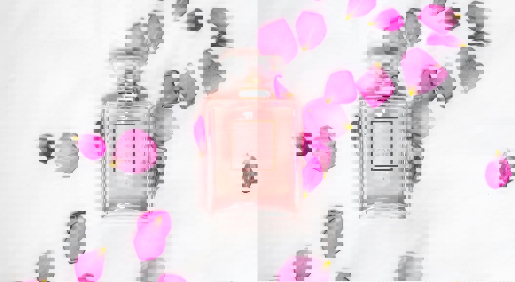 Pink perfume bottle surrounded by pink rose petals on a white background, creating an elegant and feminine aesthetic