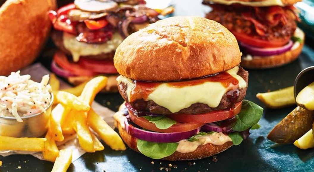 Gourmet cheeseburger med sprøstekt løk, salat og tomater på en ristet bolle, servert med en side av gyldne pommes frites i en metallkopp
