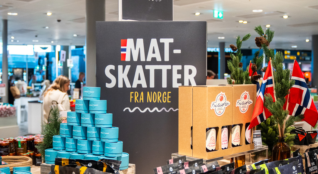 Norwegian food display in a store showcasing assorted packaged goods, including müsli and jams, with signs reading "Mat-Skatter fra Norge" and small Norwegian flags for decoration