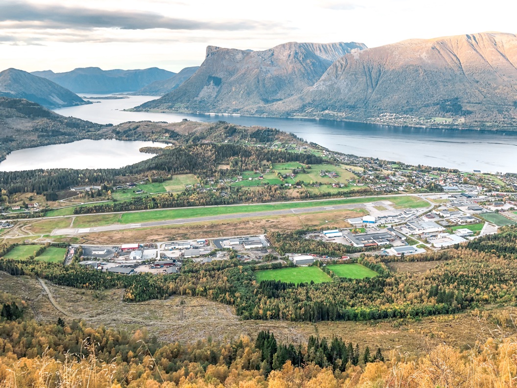 Flyfoto av Ørsta/Volda lufthavn omgitt av fjorder og fjell med grønne sletter og skogkledde åser i forgrunnen.