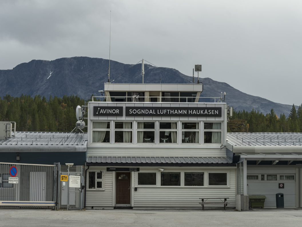 Sogndal lufthavn Haukåsen foran fjellandskap med skog i bakgrunnen, en grå dag.