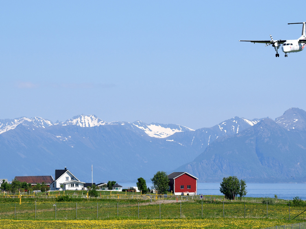 Fly som nærmer seg landingsstripen med fjellandskap i bakgrunnen og norske gårdshus i forgrunnen.