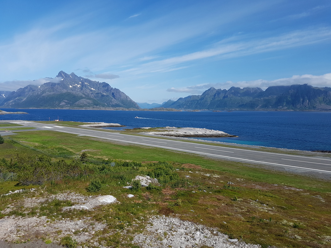 Flystripe på Svolvær flyplass ved fjord med majestetiske fjell i bakgrunnen under blå himmel i Nord-Norge.