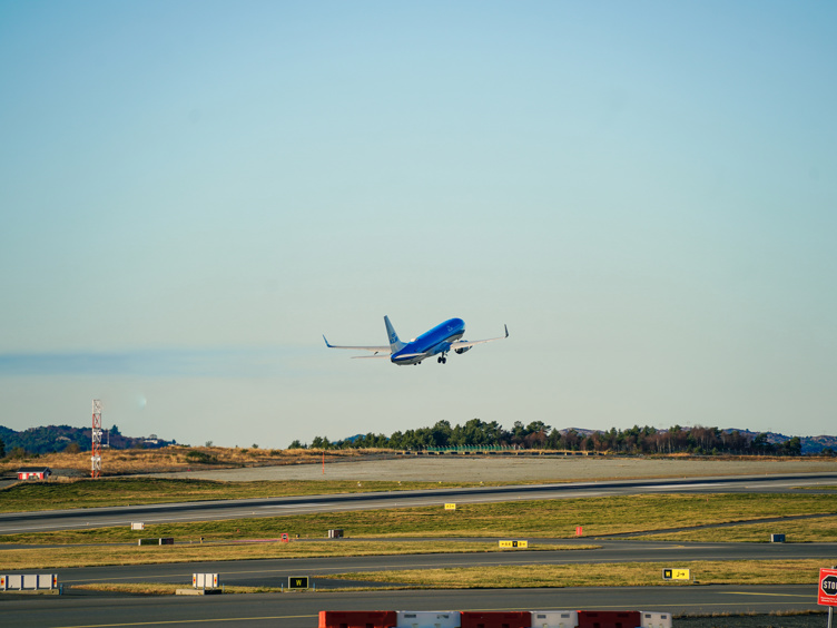 Et blått passasjerfly tar av fra rullebanen på flyplass med klar himmel i bakgrunnen.