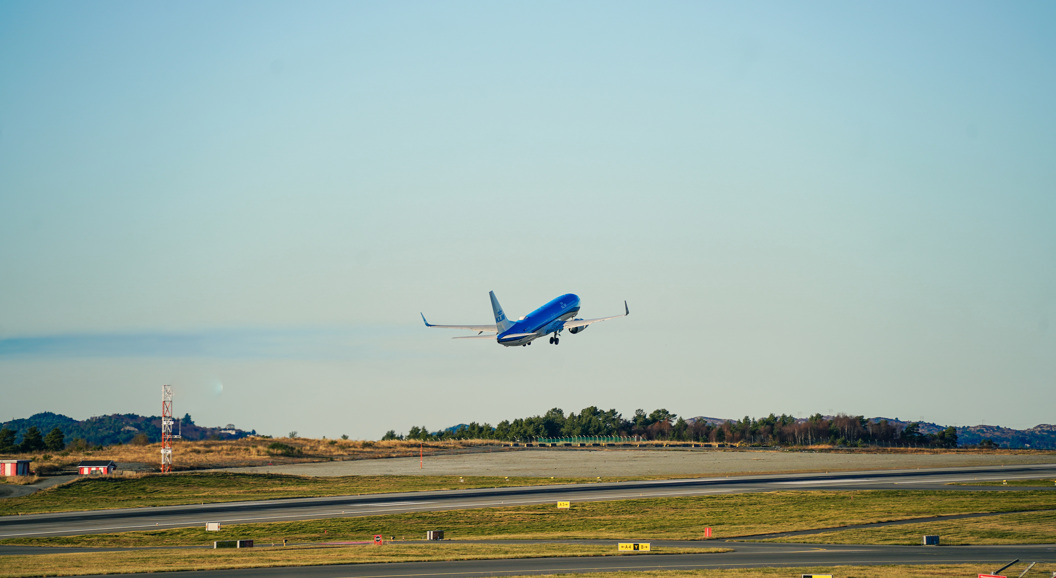 Fly som tar av fra rullebane på flyplass, klar blå himmel i bakgrunnen.