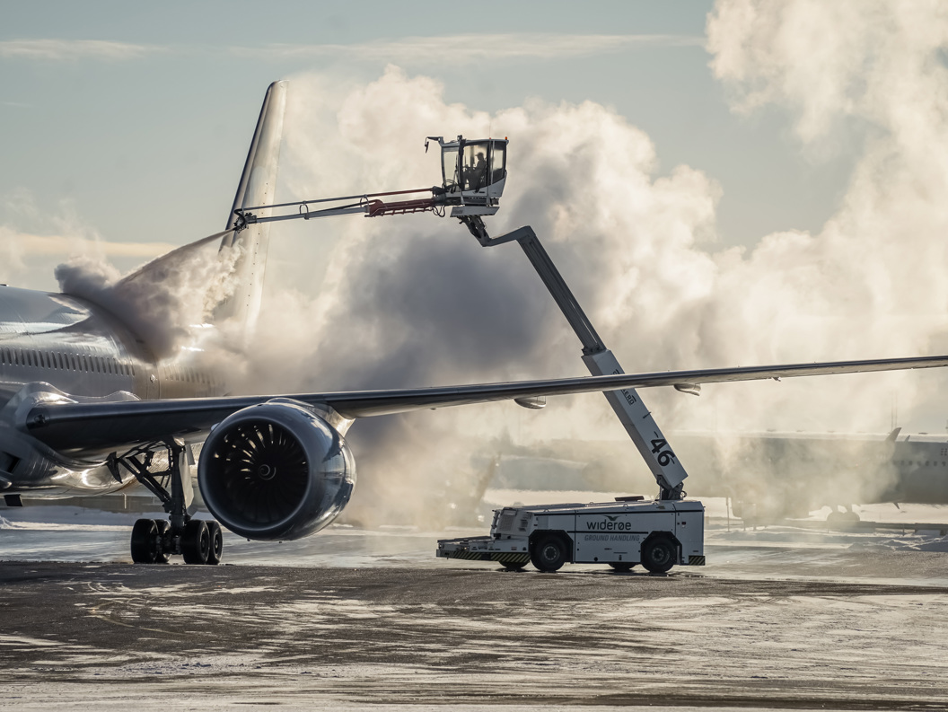 Fly gjennomgår avising på rullebanen ved bruk av spesialisert utstyr, med damp i vinteromgivelser