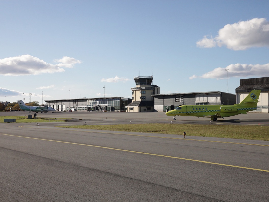 To fly på flyplassen i klart vær med flytårn og hangarer i bakgrunnen.