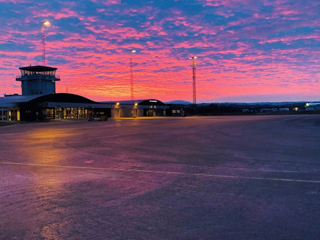 Lakselv flyplass ved solnedgang med fargerik himmel i rosa og blåtoner, terminalbygning og kontrolltårn.