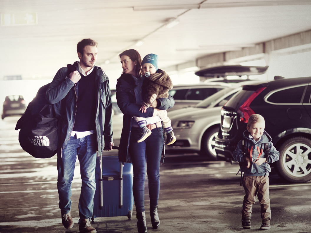 Familie med to barn på reise i parkeringshus, med bagasje og varm påkledning.