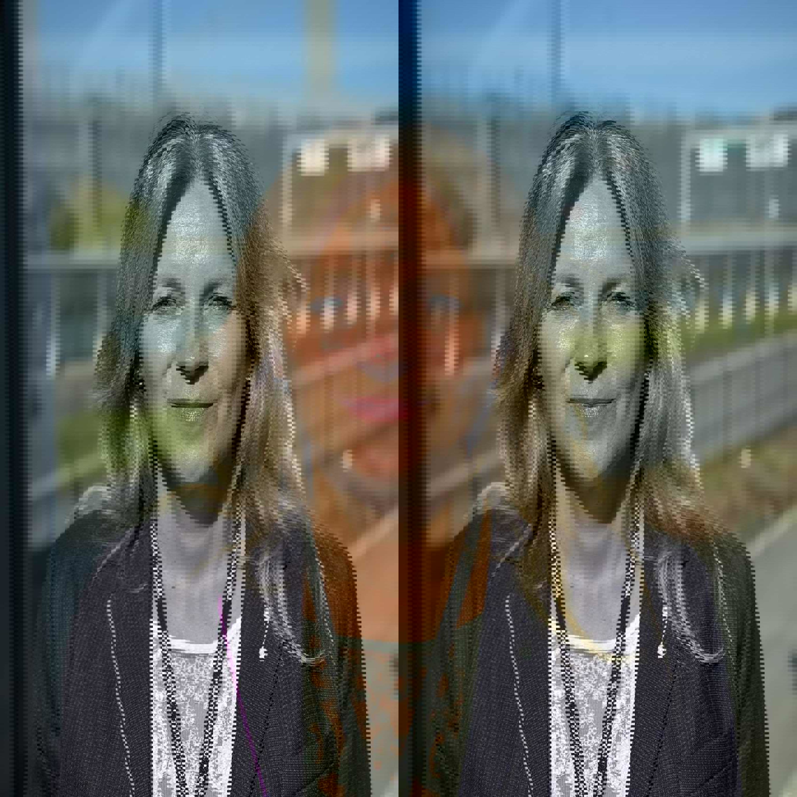 Kvinne i formelt antrekk smiler utendørs med skyfritt vær og bygninger i bakgrunnen.