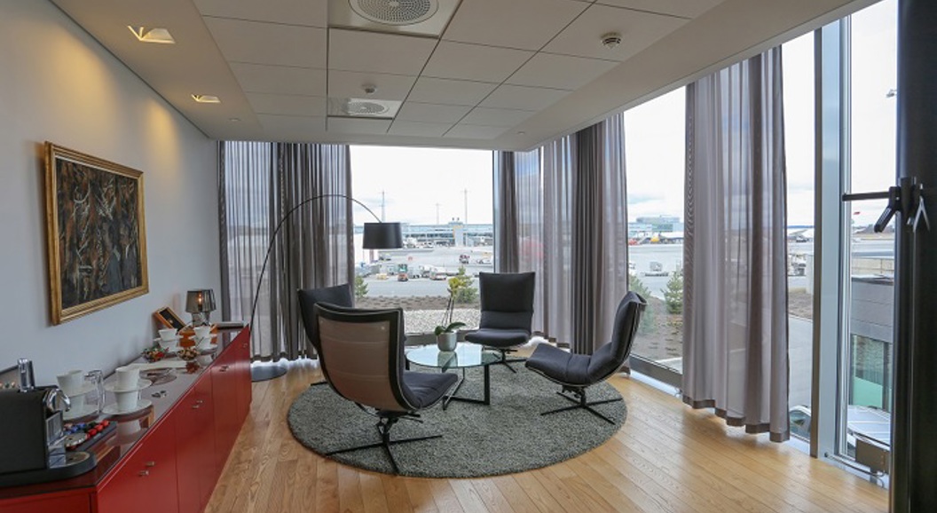 Bright meeting room with a view of the airport, elegantly decorated with modern chairs, a round table, and art on the wall.