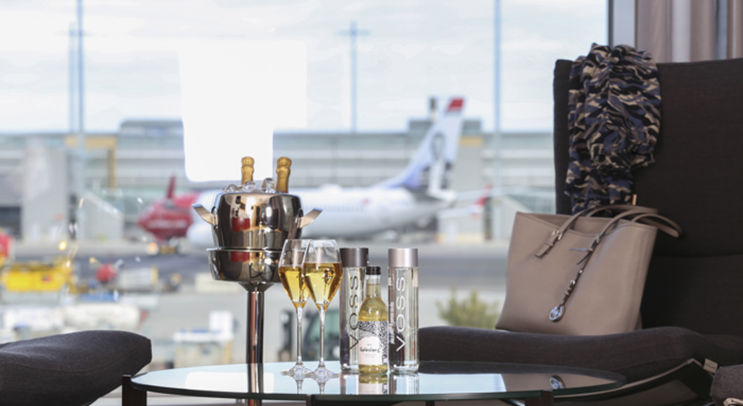 Luxurious airport lounge with a view of the runway, champagne, and Voss bottles on the table.