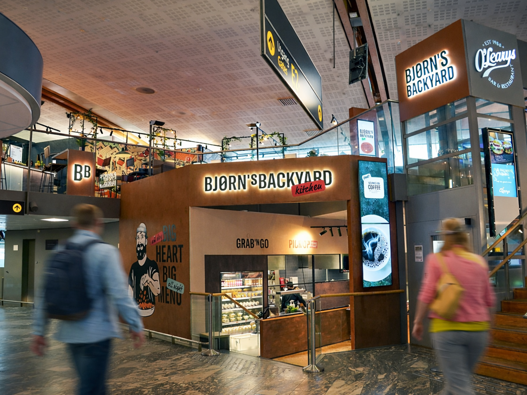 Bjørns Bakgårdskjøkken restaurantinngang i et kjøpesenter, med et veggmaleri av en skjeggete mann som holder mat, med slagordene "Stor Hjerte Stor Meny" og "Grab 'N Go, Pick Up