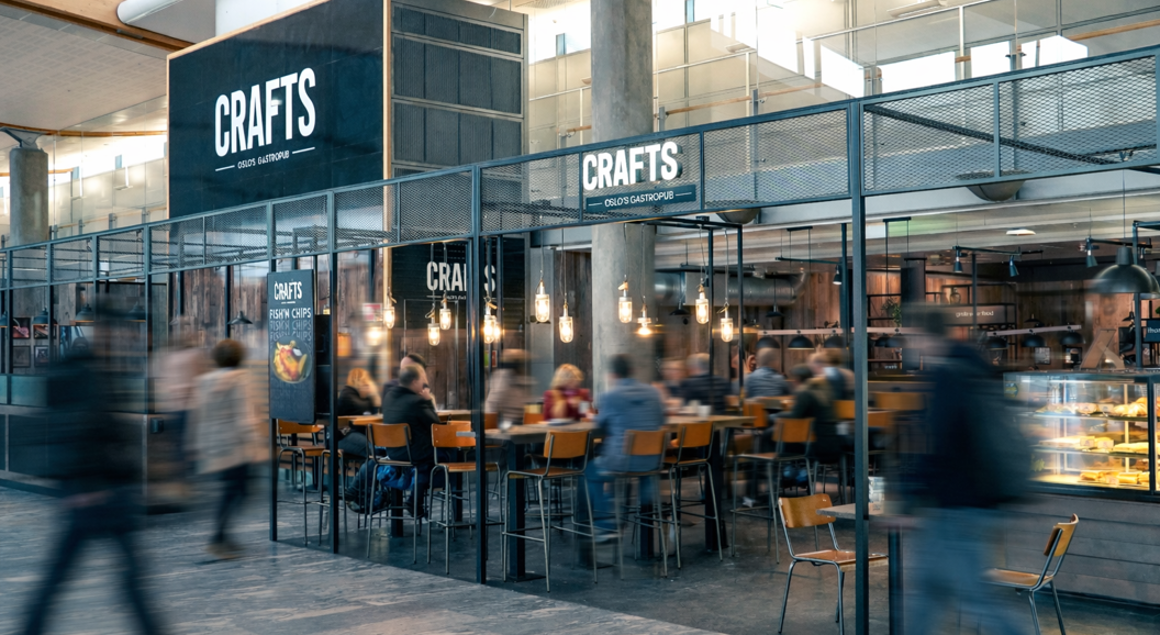 Gourmetburger og søtpotetfries med et glass øl på et bord i en flyplasslounge, fly synlig i bakgrunnen