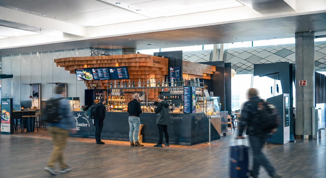 Moderne barinteriør med treinnslag og slankt design på Hunter Bar, som viser en digital meny, hengende glass og en utstillingsmonter med matvarer