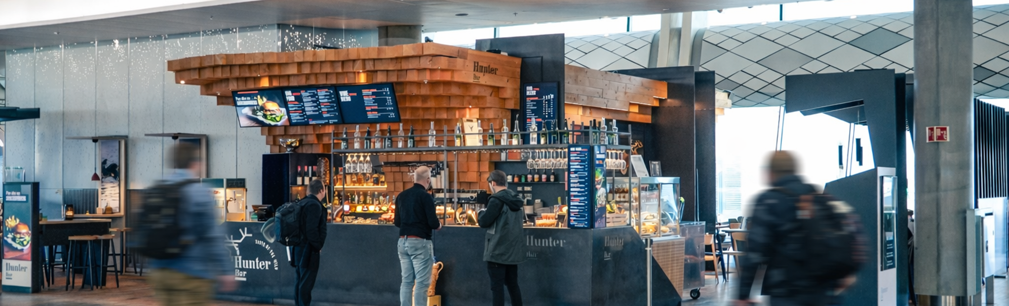 Moderne barinteriør med treinnslag og slankt design på Hunter Bar, som viser en digital meny, hengende glass og en utstillingsmonter med matvarer