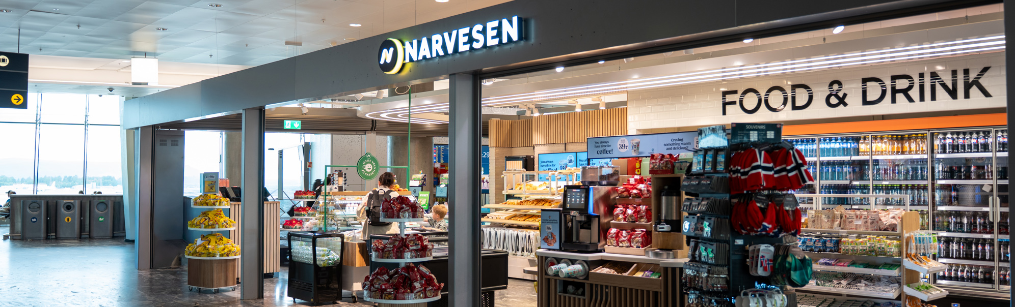 Moderne Narvesen-kiosk på en flyplass som tilbyr nødvendighetsartikler, snacks og drikkevarer under levende belysning