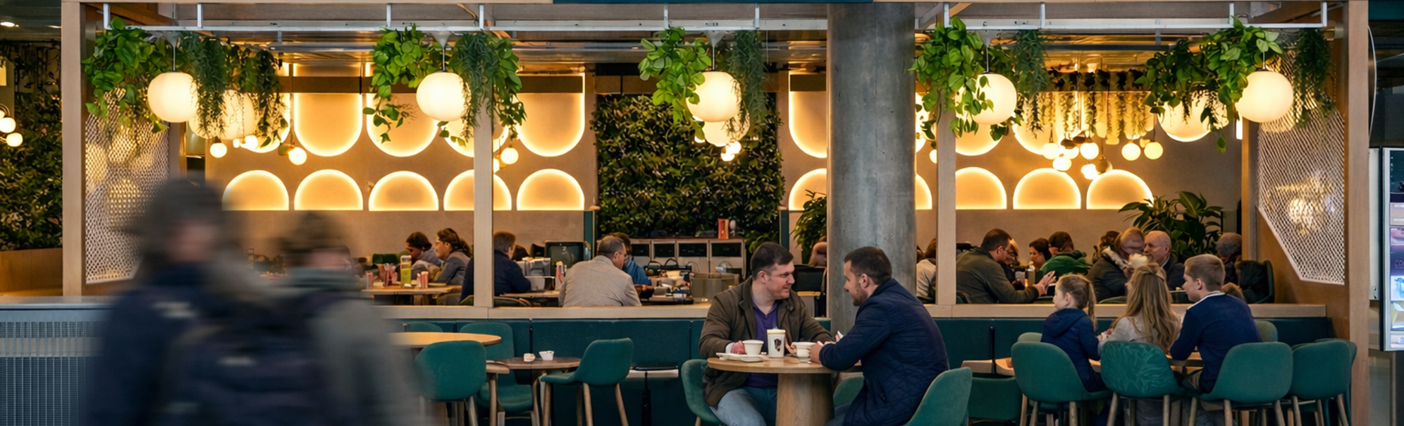 Moderne kafé og spiseområde med stilige sitteplasser, grøntområder og stemningsbelysning, med seksjoner for kaffe og frokost, samt lunsj og middag