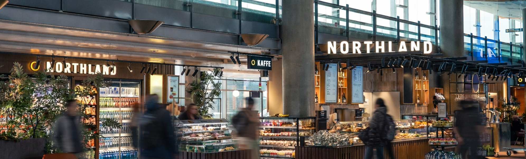 Folk som ser på matutvalg ved en moderne flyplassdelidisk med forskjellige pakkede varer og ferske produkter