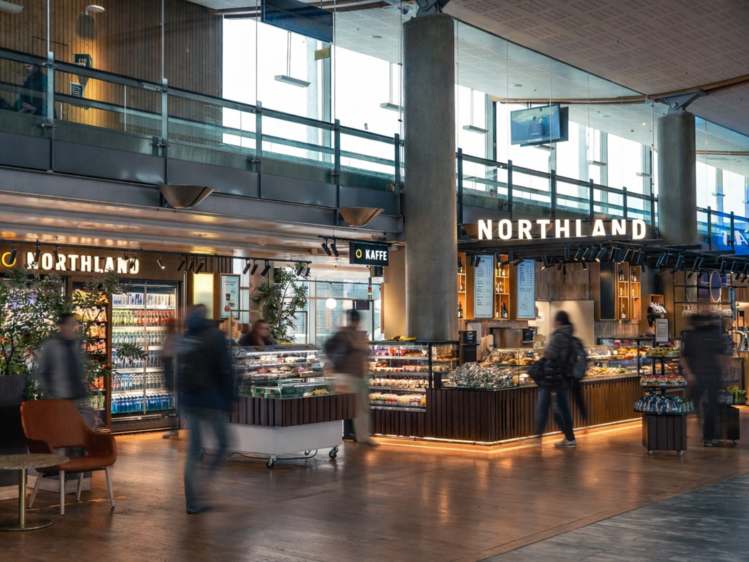 Folk som ser på matutvalg ved en moderne flyplassdelidisk med forskjellige pakkede varer og ferske produkter