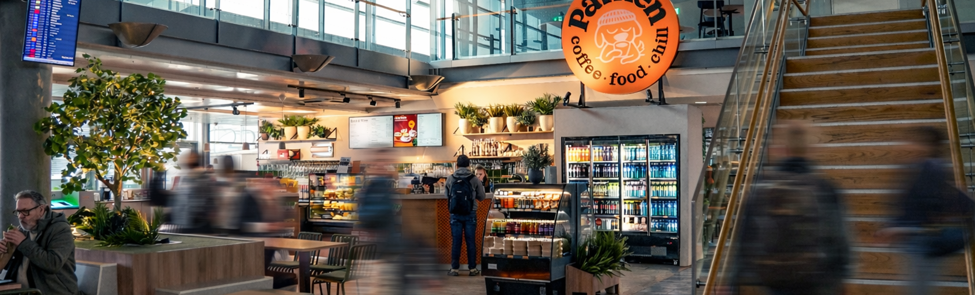 Interiør i en flyplasskafé med et skilt som reklamerer for spaghetti bolognese for 115 valutaenheter; kaféen heter Parken og har en avslappet atmosfære med sitteplasser og planter